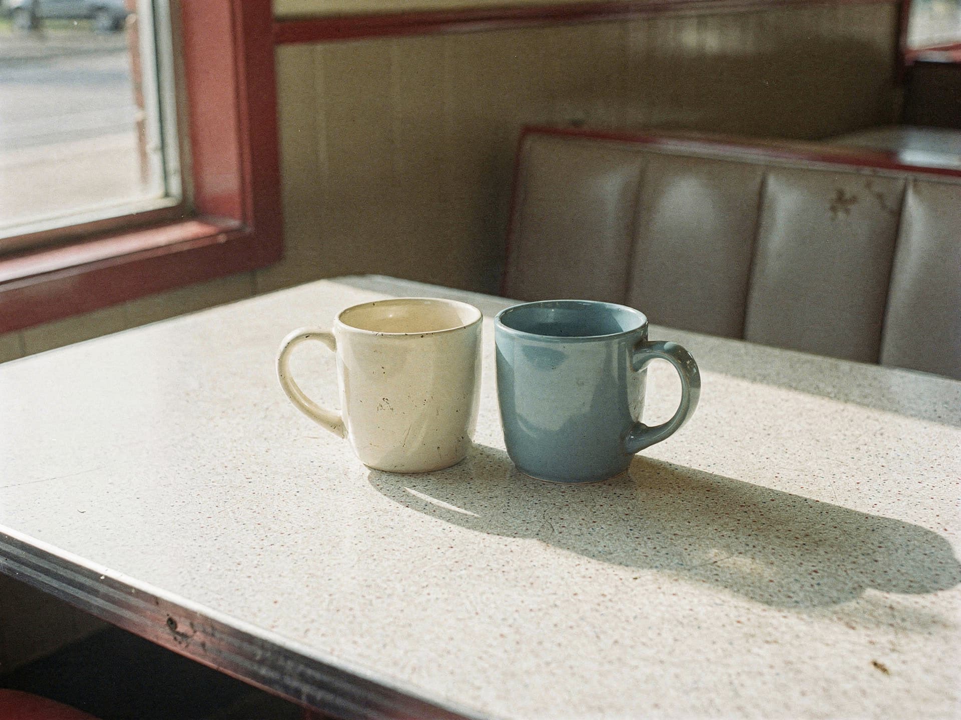 Two coffee mugs side by side on a sunlit diner table