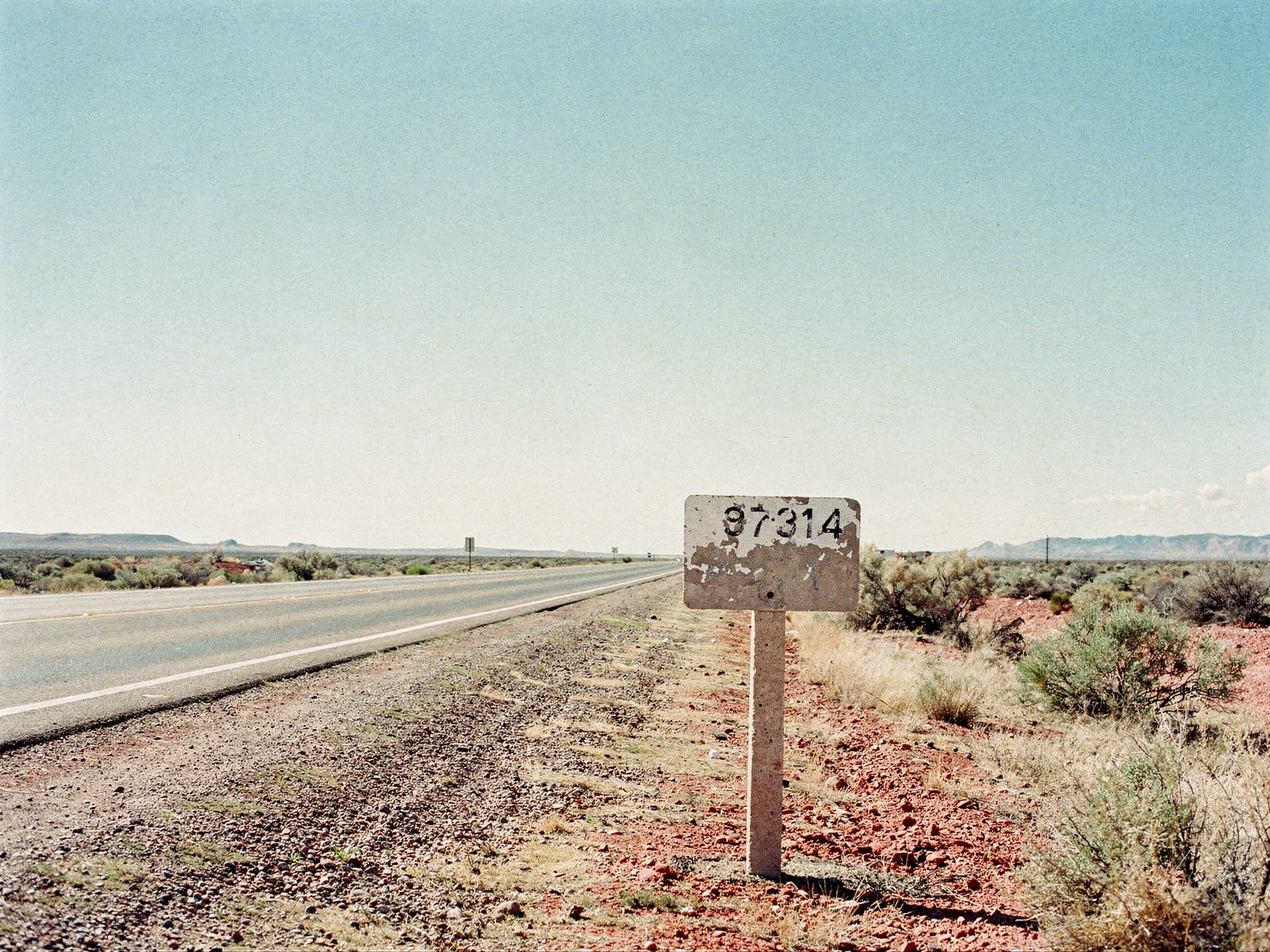 A concrete roadside mileage marker on a quiet desert highway