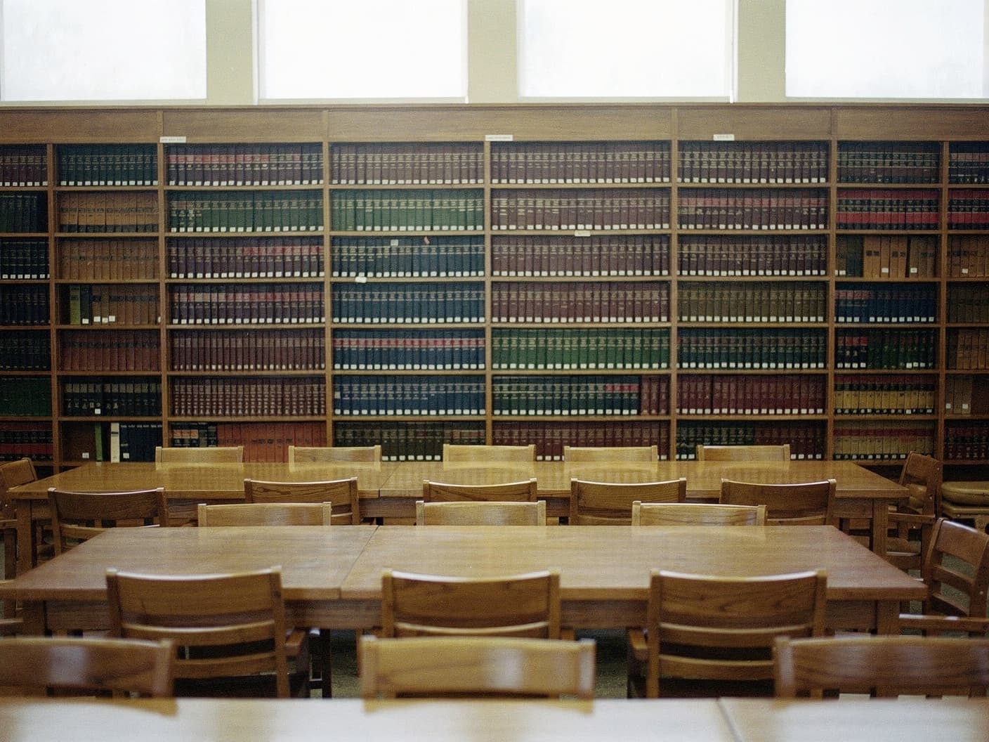 A quiet municipal library reading room with oak study tables and bookshelves in deep focus